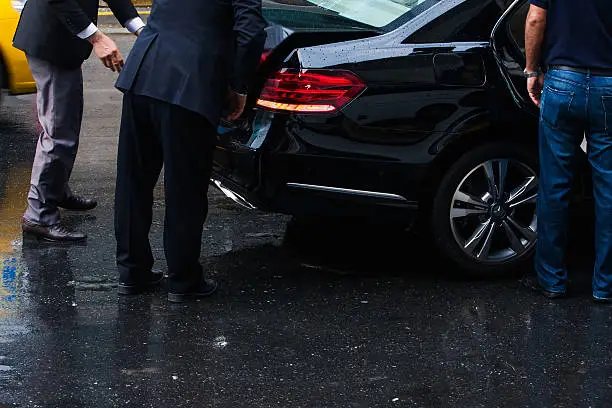 Driver with assistant met the businessman at the airport in London. luxury Mercedes sedan. rainy day
